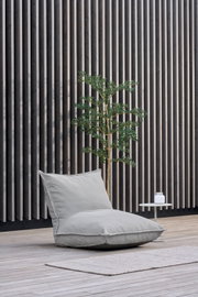 Lichtgrijze zitzak-loungestoel met rugleuning op een houten terras voor een verticale wand van houten lamellen, zijaanzicht