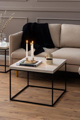 Moderner Couchtisch mit heller Holzplatte und schwarzem Metallgestell, dekoriert mit Kerzen und Tasse, seitliche Perspektive.