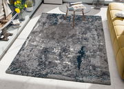 Moderner Teppich in Grau- und Blautönen, rechteckig, auf einem hellen Boden in einem stilvollen Wohnzimmer mit gelbem Sofa und Glastisch, von oben betrachtet.