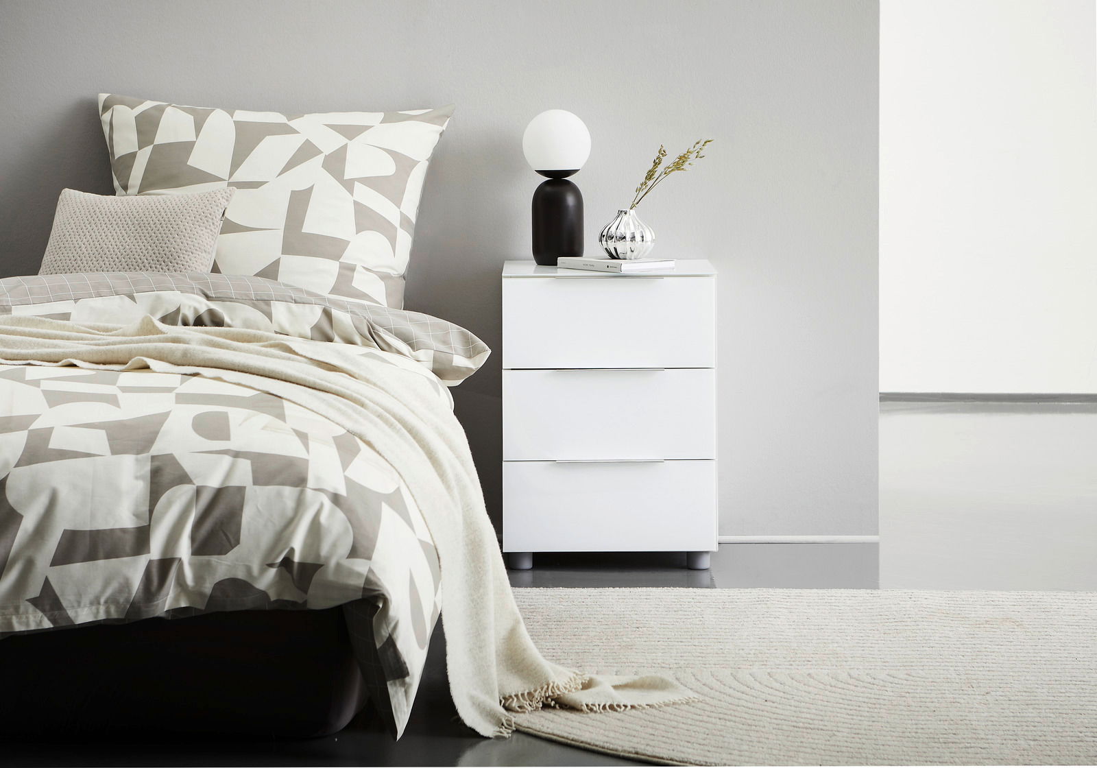 Weiße Nachtkonsole mit drei Schubladen, dekoriert mit einer Lampe und einer Vase, seitliche Perspektive