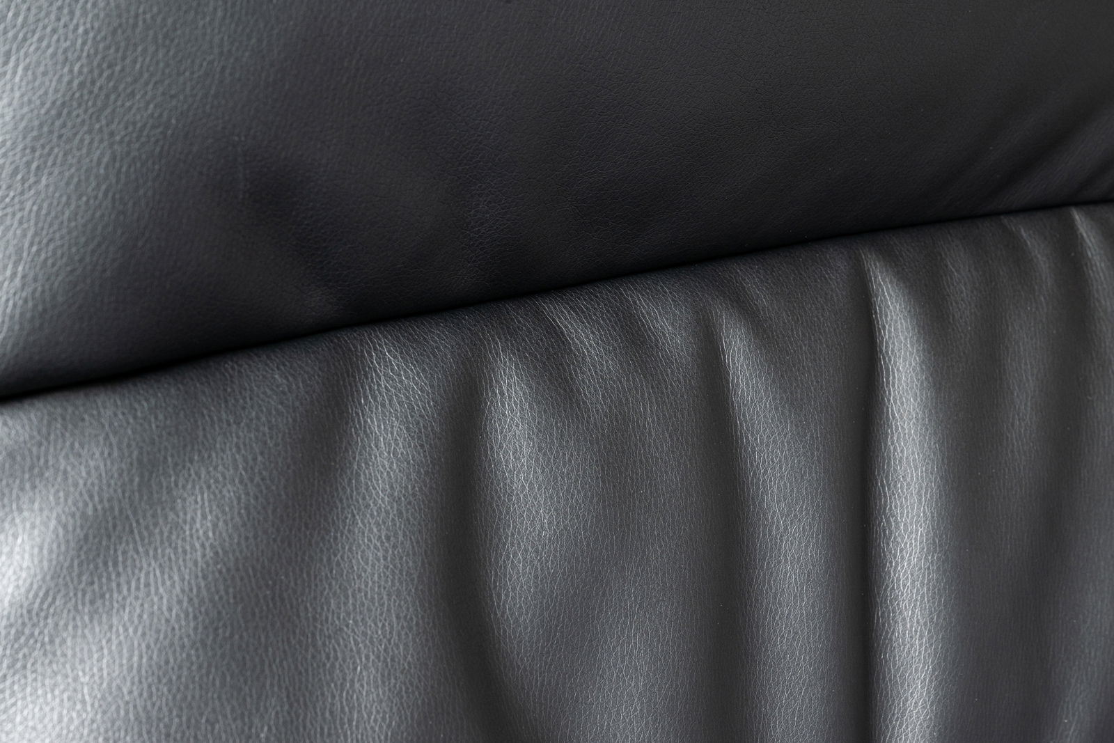 Nahaufnahme der schwarzen Lederpolsterung eines Chefsessels, von vorne betrachtet.