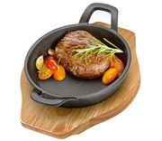 Servierpfanne mit Griffen, gefüllt mit einem saftigen Steak und frischen Tomaten, auf einem Holzbrett von oben betrachtet.