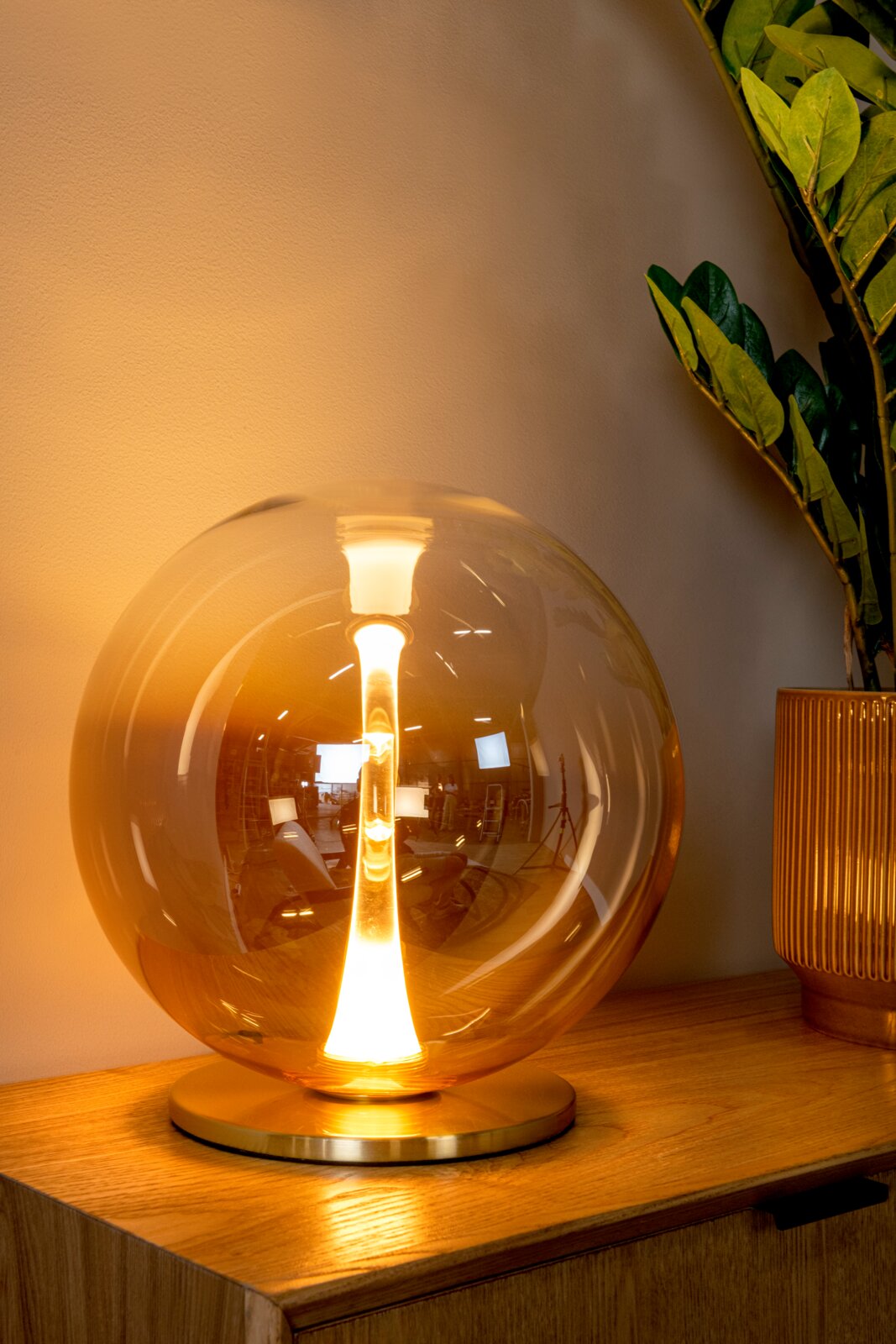 Leuchtende Tischlampe mit großer runder Glas-Kuppel und warmweißem Licht auf Holzoberfläche, schräg von vorne fotografiert