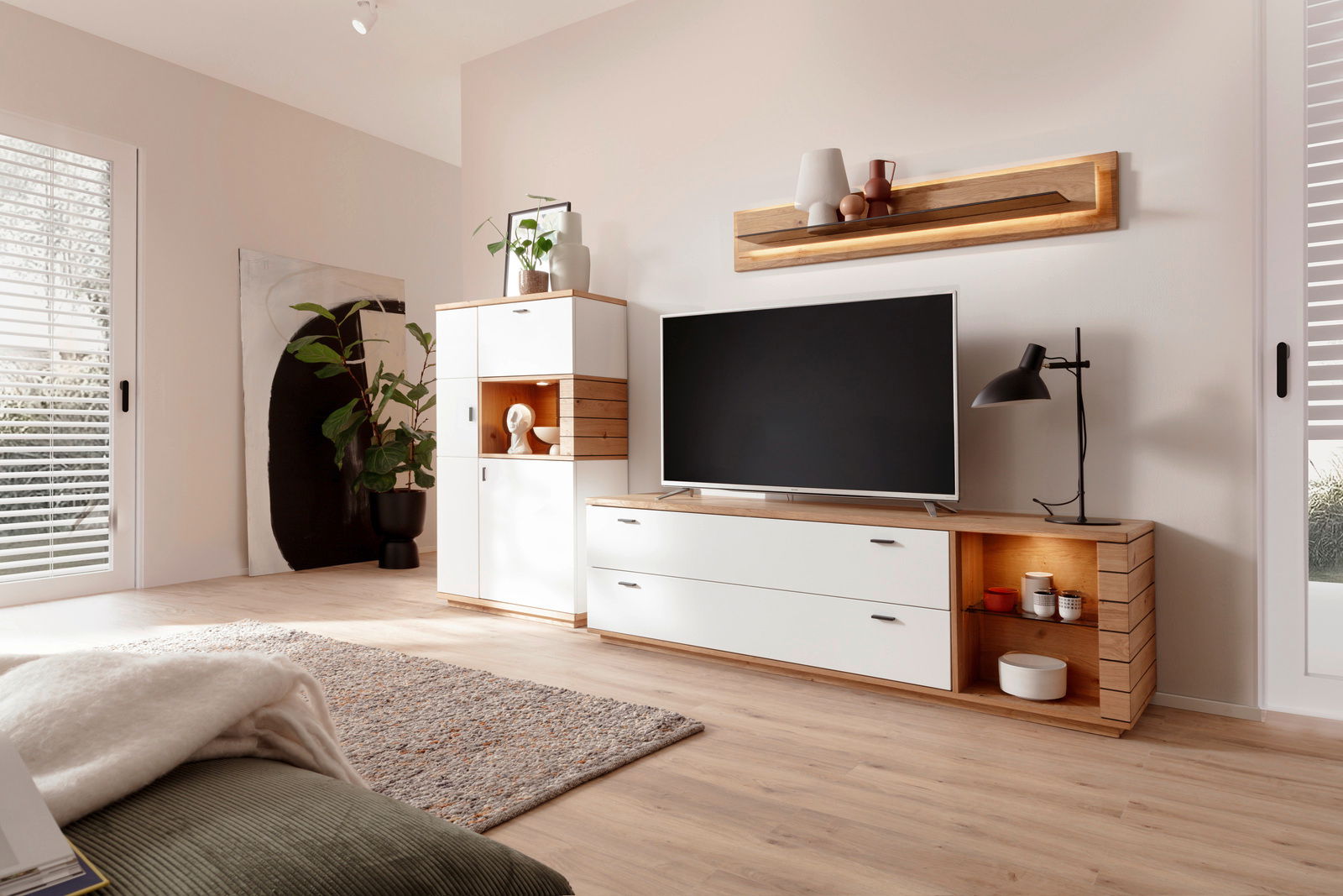 Moderne Wandkombination in einem hellen Wohnzimmer, bestehend aus einem weißen TV-Schrank mit Holzdetails und einem hohen Schrank mit dekorativen Elementen. Perspektive von schräg vorne.