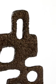 Detailopname in vooraanzicht van een abstract donkerbronskleurig object met een robuuste textuur en organische geometrische uitsparingen tegen een witte achtergrond