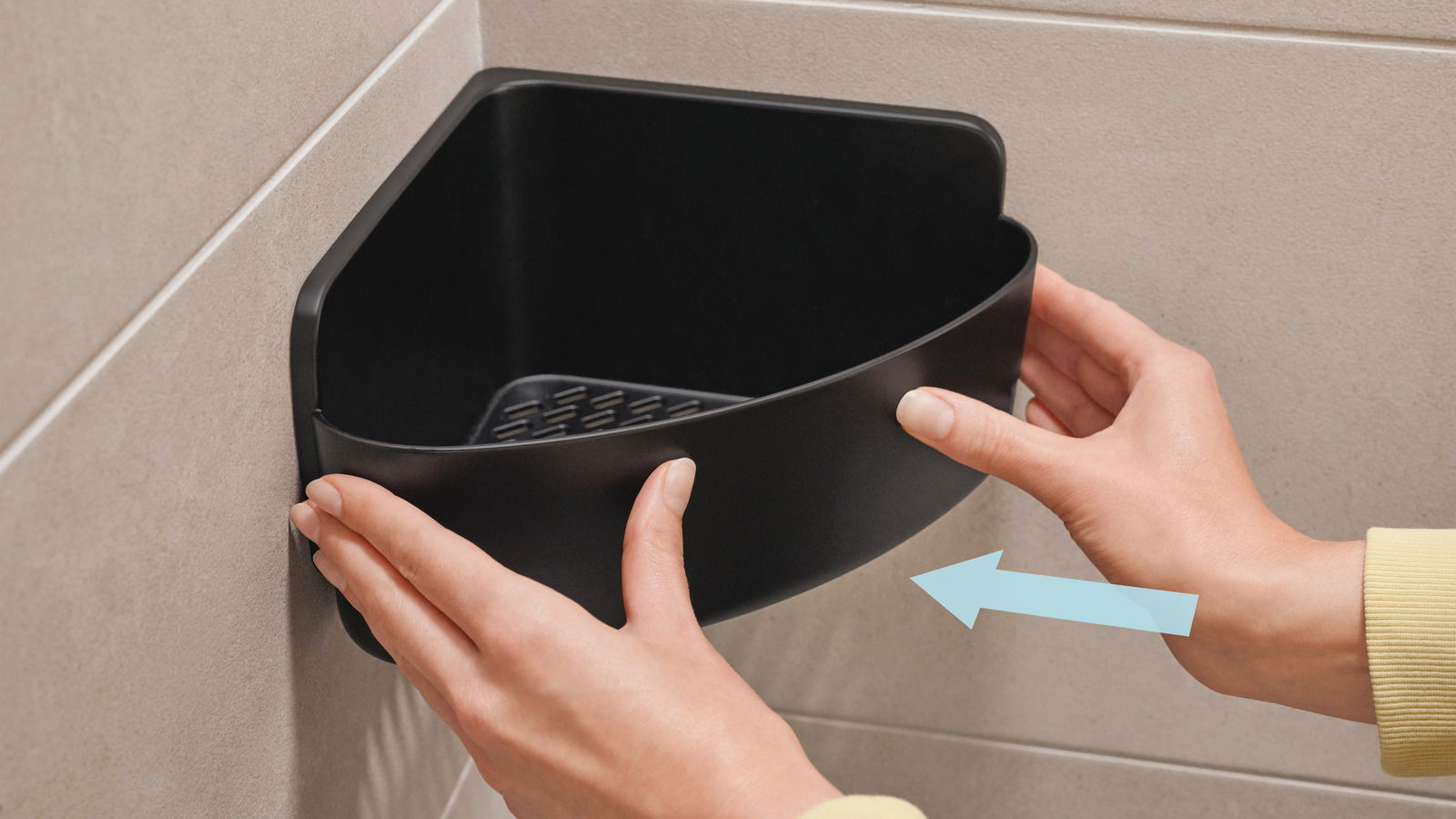 Schwarzer Eckduschkorb von tesa Lavaa, der in einer Ecke an der Wand montiert wird. Perspektive von vorne mit Händen, die den Korb halten.