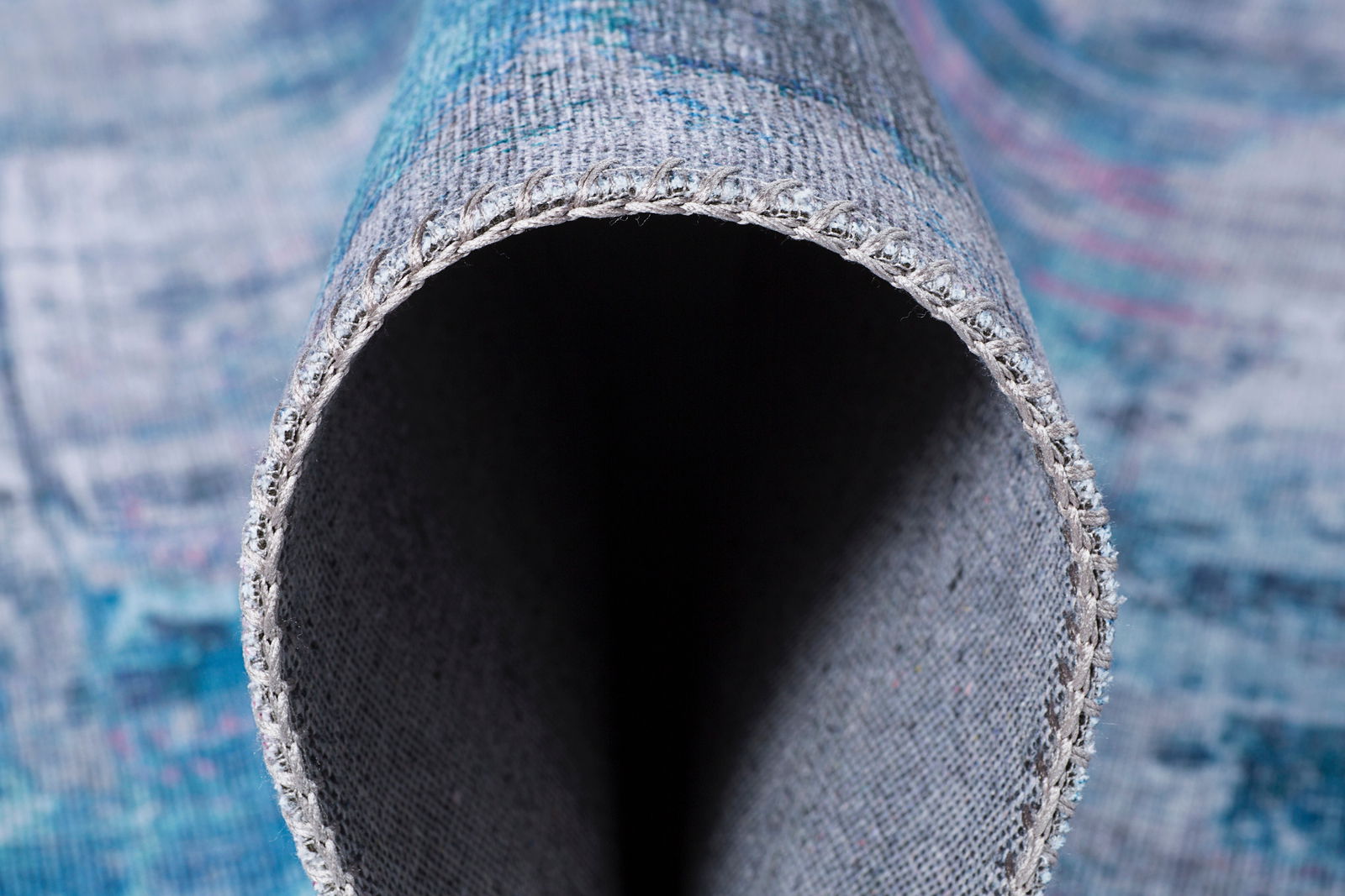 Nahaufnahme eines zusammengerollten Teppichs mit sichtbarer Kante und Textur, Perspektive von der Seite.