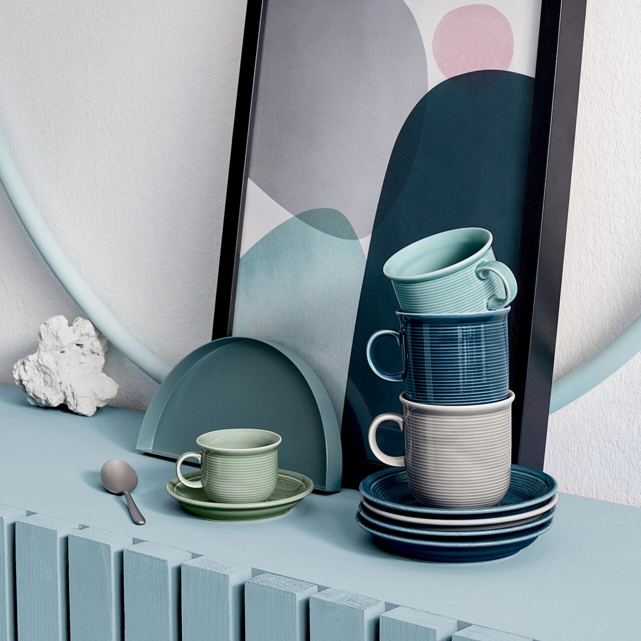 Thomas Kaffeebecher Trend Colour Stapel von Tassen in verschiedenen Grautönen und Blau, auf einem Tisch mit dekorativem Hintergrund, seitliche Perspektive