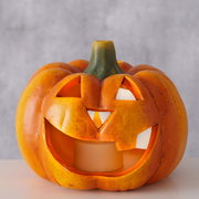 Teelichthalter in Form eines Kürbisses mit geschnitztem Gesicht, frontal fotografiert.