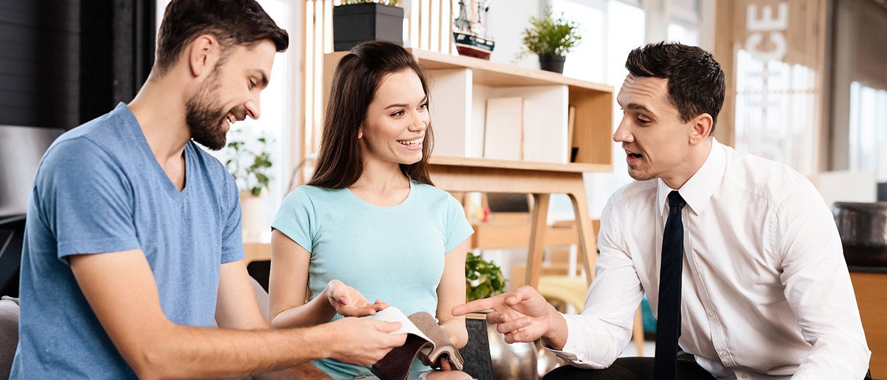 Ein Paar spricht mit einem Berater, während der Mann eine Stoffauswahl in der Hand hält.