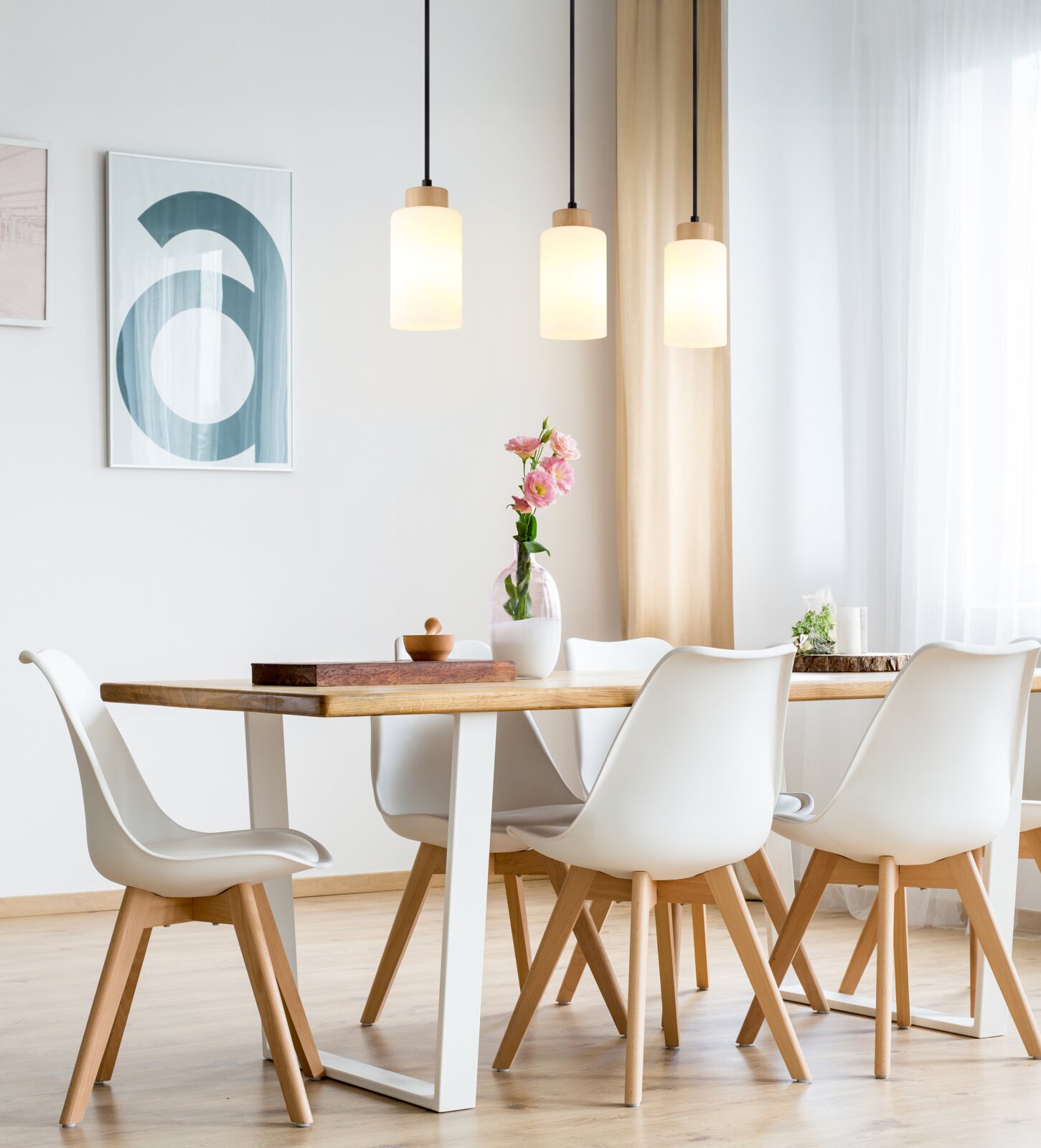 Lichte eetkamer met een houten tafel en vier witte stoelen, daarboven drie cilindervormige hanglampen met houten details vooraanzicht van de tafelset