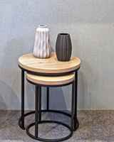 Zwei runde Beistelltische aus Holz mit schwarzem Metallgestell, übereinander gestapelt, mit zwei dekorativen Vasen darauf, seitliche Perspektive.