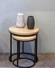 Zwei runde Beistelltische aus Holz mit schwarzem Metallgestell, übereinander gestapelt, mit zwei dekorativen Vasen darauf, seitliche Perspektive.