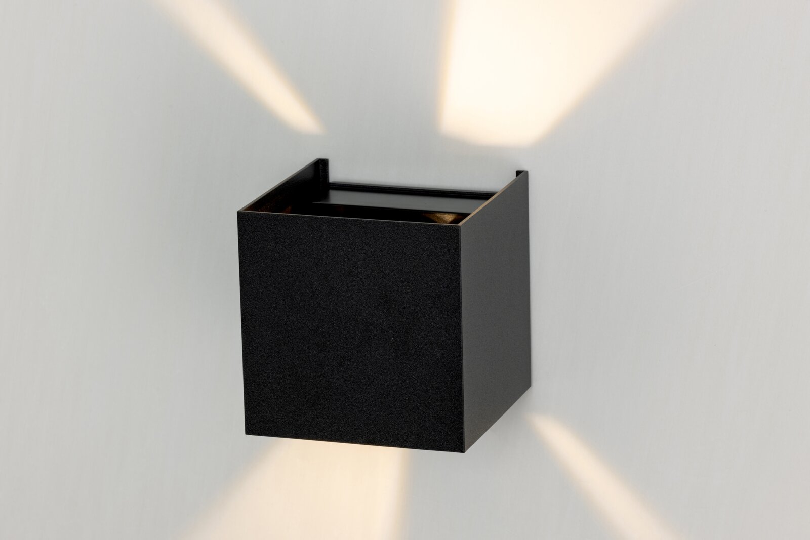 Zwarte LED-wandlamp in de vorm van een kubus, die vanaf de zijkant wordt bekeken en lichtstralen naar boven en beneden verspreidt.