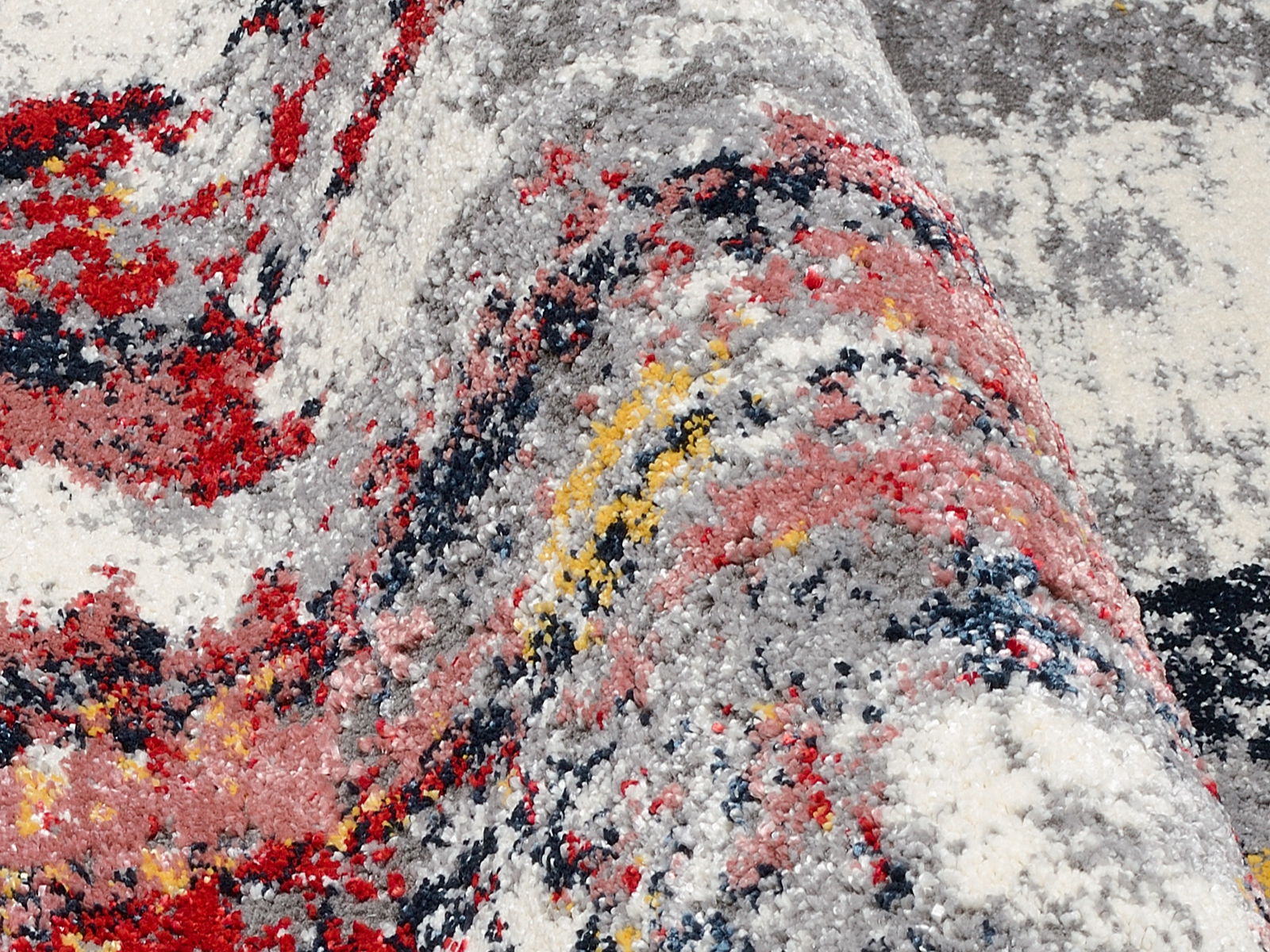 Nahaufnahme eines Designer-Teppichs mit abstraktem Muster in Rot, Grau, Gelb und Weiß, aus seitlicher Perspektive aufgenommen.