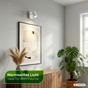 Witte verstelbare wandspot met warmwit licht, schuin van voren getoond boven een kunstwerk in een stijlvol interieur.