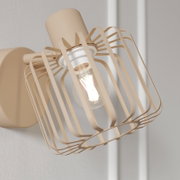 Beige Wandlampe mit modernem Drahtgitter-Schirm und sichtbarer, leuchtender Filament-Glühbirne, seitliche Nahaufnahme in leichter Untersicht.