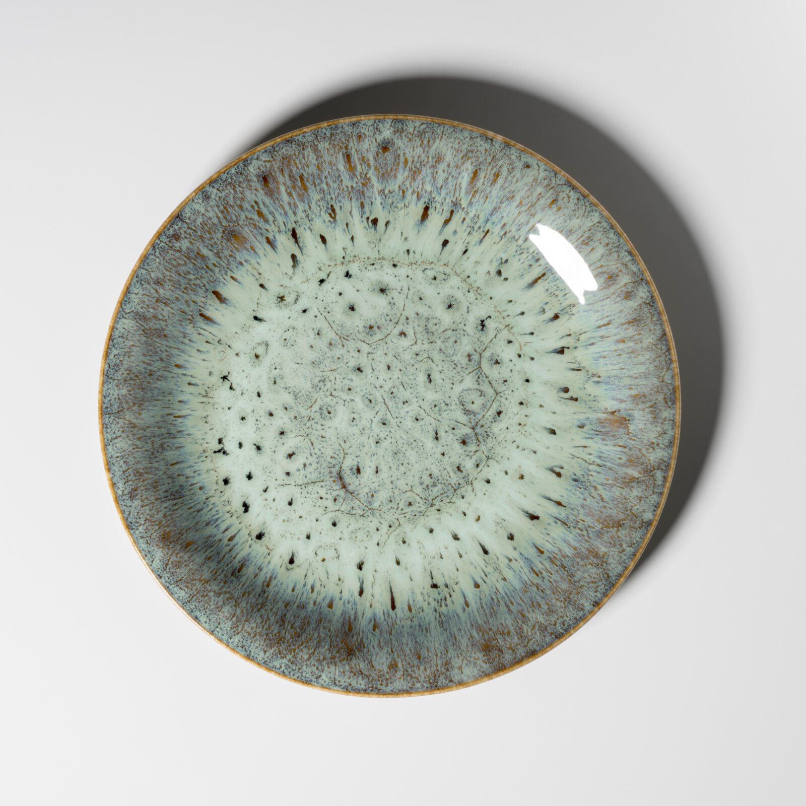 Runde Keramikschale mit blau-grün gesprenkelter Glasur und braunem Rand, Draufsicht von oben auf weißem Hintergrund