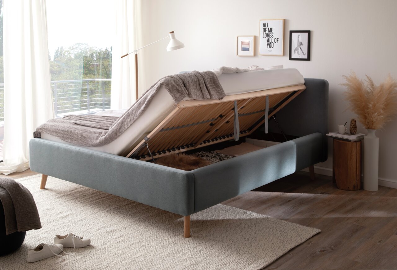 Polsterbett mit Stauraumfunktion, seitliche Perspektive, hochgeklappte Matratze, modernes Design, helle Umgebung