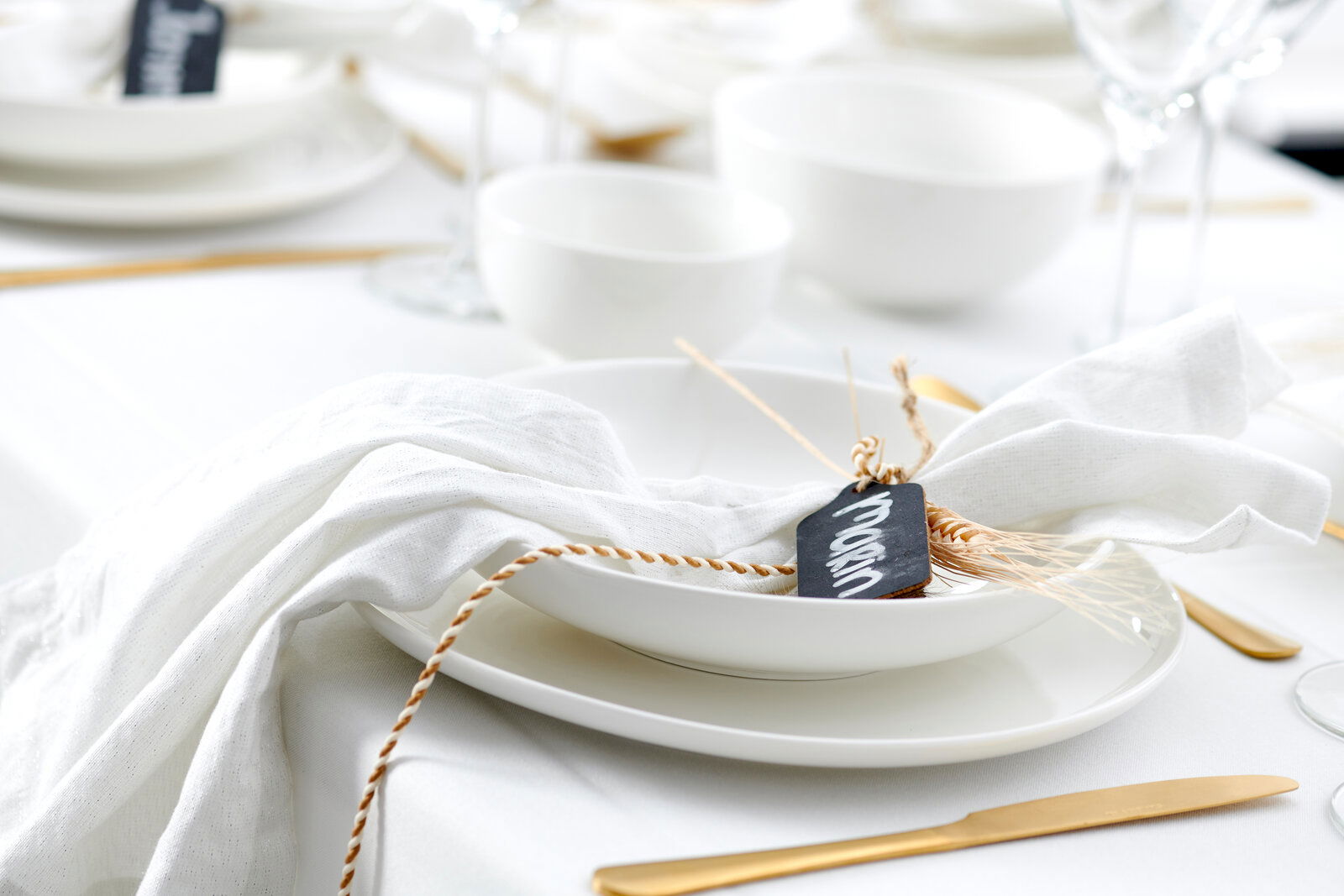 Eleganter Speiseteller Skagen 30,5 cm, von oben fotografiert, auf einem gedeckten Tisch mit weißem Tischtuch und goldfarbenem Besteck, dekoriert mit einer Serviette und einem Namensschild.
