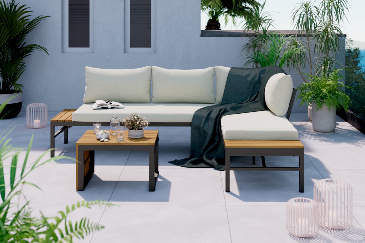 Moderne loungeset op een terras met planten op de achtergrond, bestaande uit een hoekbank met lichte kussens en een kleine houten tafel, gezien vanuit de zijkant.