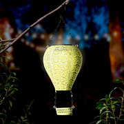 Metallener Solarballon in Form eines Heißluftballons, aufgehängt an einem Ast, leuchtet in der Dämmerung. Perspektive von vorne.