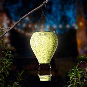 Metallener Solarballon in Form eines Heißluftballons, aufgehängt an einem Ast, leuchtet in der Dämmerung. Perspektive von vorne.