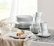 Elegantes Kombiservice Lido Black 30-teilig, bestehend aus Tellern, Tassen und Schalen, auf einem gedeckten Tisch mit einem Glas Weißwein und einem Teller mit Lachsgericht, seitliche Perspektive.