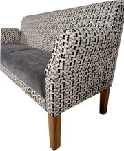 Nahaufnahme eines gepolsterten Sofas mit gemustertem Stoff in Schwarz/Grau/Beige, grauer Sitzfläche und Holzbeinen, gezeigt aus schräger Vorderseitenperspektive mit Fokus auf Armlehne und Rückenlehne