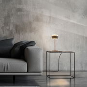 Moderne Akku-Tischleuchte auf einem minimalistischen Beistelltisch neben einem grauen Sofa, seitliche Perspektive.