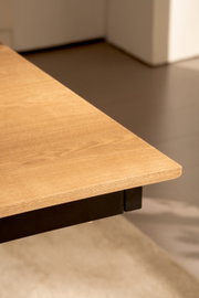 Detailaufnahme einer rechteckigen Tischplatte in heller Holzoptik mit abgerundeter Kante und schwarzem Metallgestell, perspektivisch von oben schräg auf eine Ecke fotografiert
