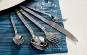 Elegantes 30-teiliges Besteckset aus Edelstahl mit gedrehten Griffen, auf blauer Tischdecke von oben fotografiert.