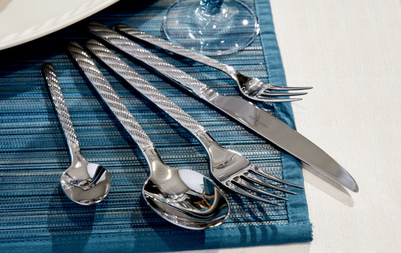 Elegantes 30-teiliges Besteckset aus Edelstahl mit gedrehten Griffen, auf blauer Tischdecke von oben fotografiert.