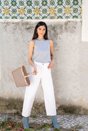 Frau in weißer Hose und grauem Top hält einen kleinen, beigen Korb in der Hand, seitliche Perspektive.