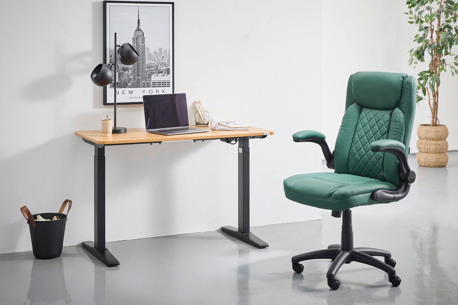 Moderner E-Schreibtisch mit Holzplatte und schwarzen Metallbeinen, seitliche Perspektive. Auf dem Tisch stehen eine schwarze Lampe, ein Laptop und Schreibutensilien. Daneben ein grüner Bürostuhl auf Rollen.