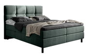 Boxbed in zijaanzicht met een gestoffeerd hoofdeinde en elegante kussens en dekens.