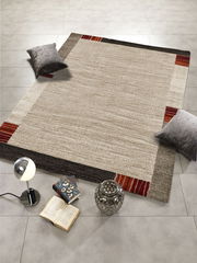 Moderner Teppich in Beige- und Brauntönen mit roten Akzenten, dekoriert mit Kissen, Büchern und einer Lampe, aus der Vogelperspektive fotografiert.