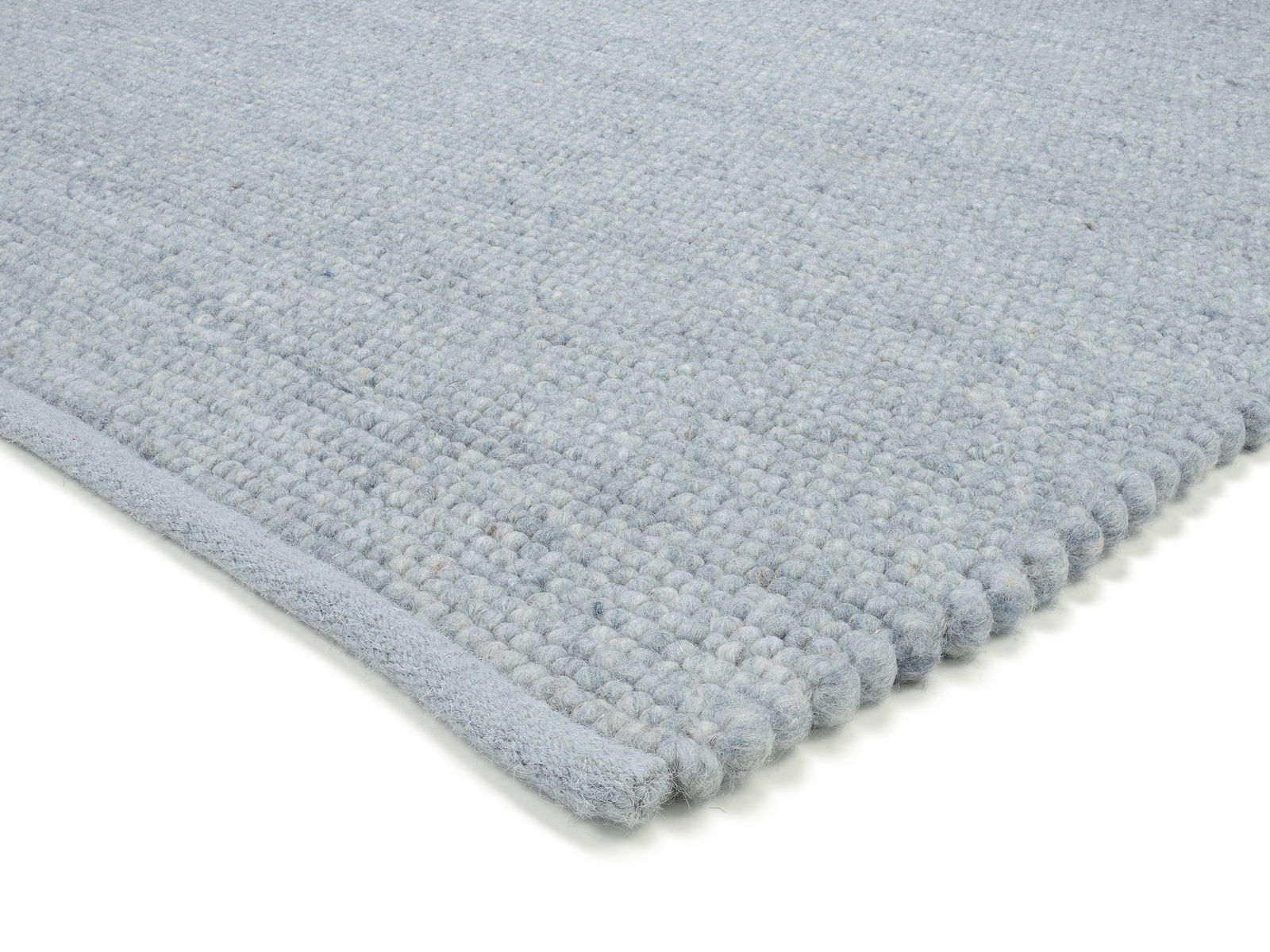 Nahaufnahme eines handgewebten Teppichs in hellblauer Farbe, der die Textur und die Kanten des Teppichs zeigt.