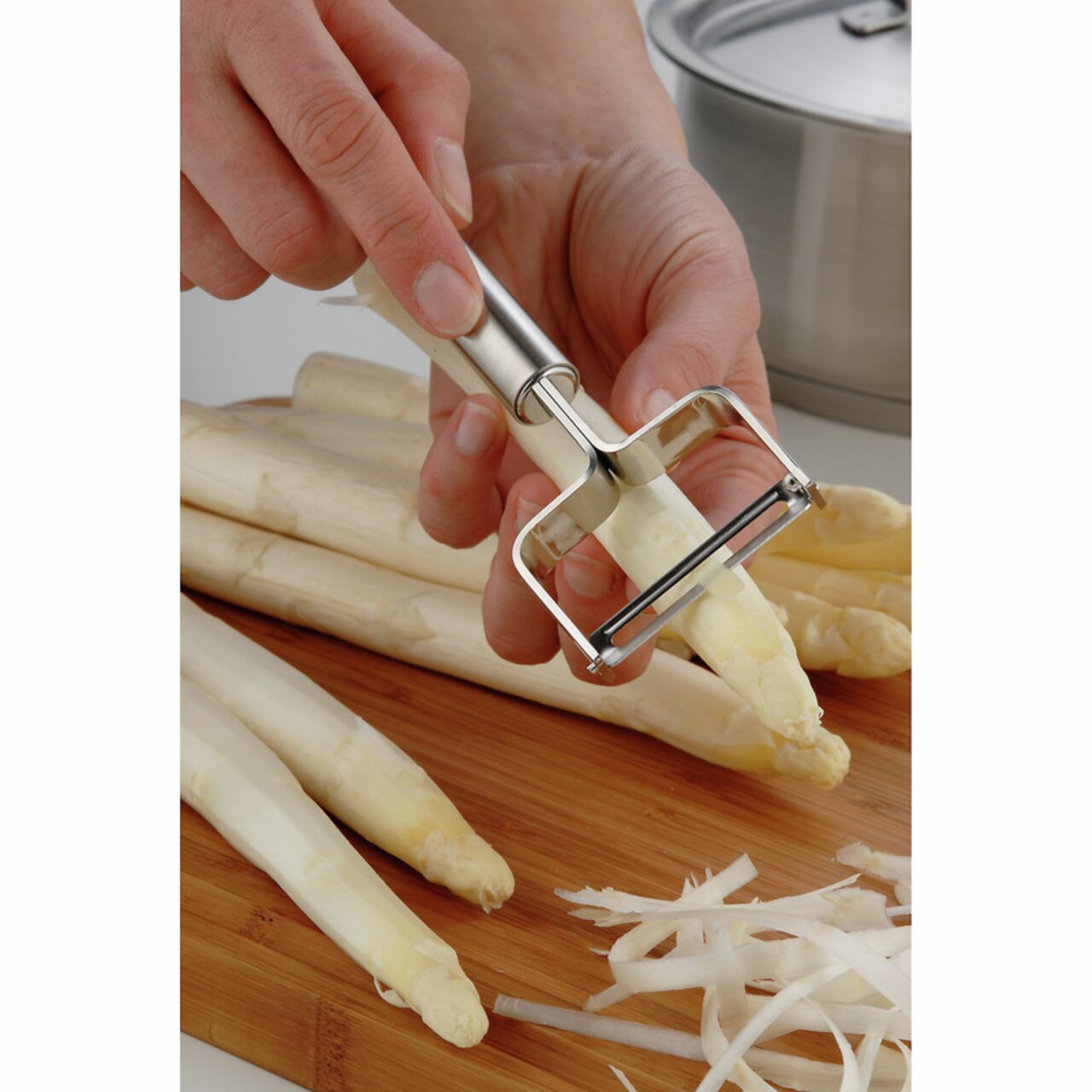 Nahaufnahme eines Sparschälers PROFI PLUS, der weißen Spargel auf einem Holzbrett schält.