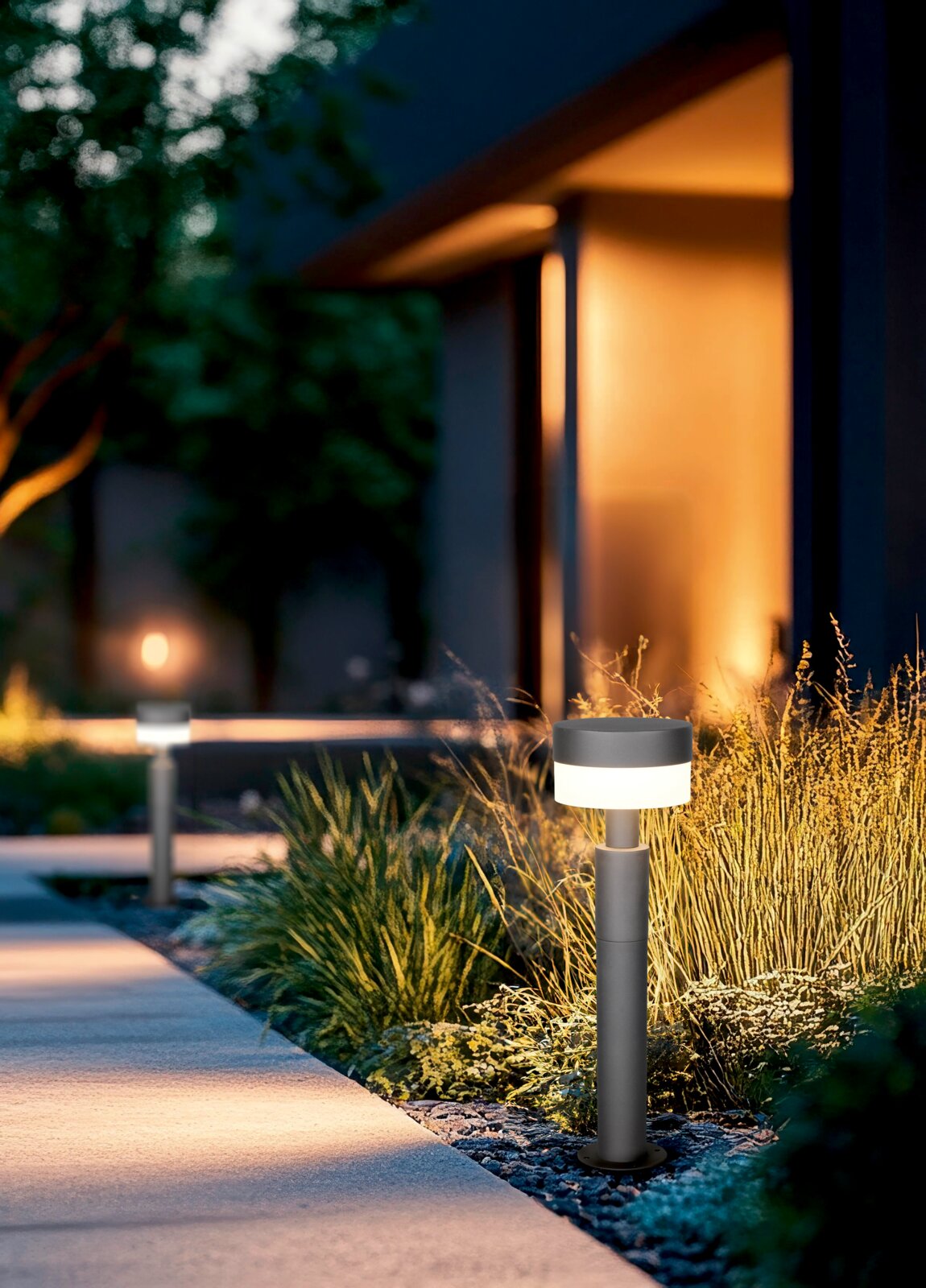 Moderne LED-Pollerleuchte in einem Garten bei Dämmerung, seitliche Perspektive