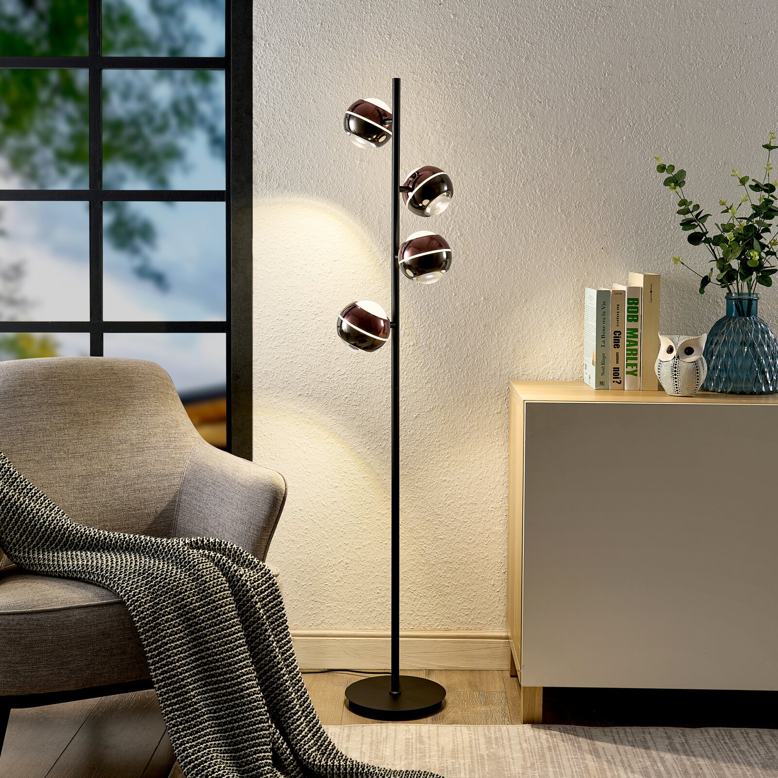 Moderne schwarze Stehleuchte mit vier kugelförmigen, rauchglasfarbenen Lampenschirmen im Wohnzimmer, seitliche Perspektive