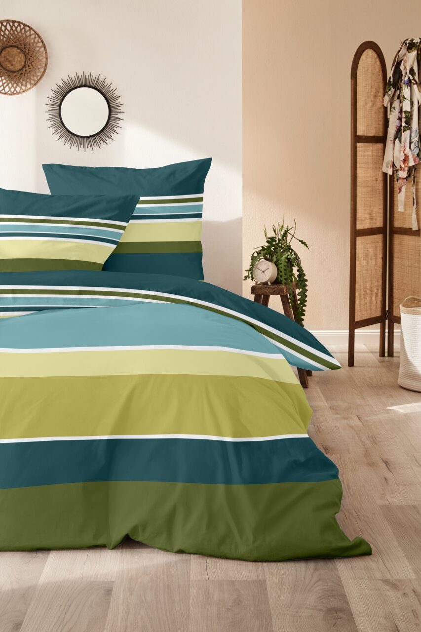 Gestreifte Bettwäsche in Petrol, Türkis und Olivgrün mit passenden Kissen auf einem Bett im Schlafzimmer, Frontansicht leicht schräg von links.