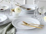 Elegant gedeckter Tisch mit weißen Porzellantellern, goldfarbenem Besteck und Kristallgläsern, dekoriert mit weißen Blumen – Perspektive: leicht von oben, schräger Blick auf das Gedeck.