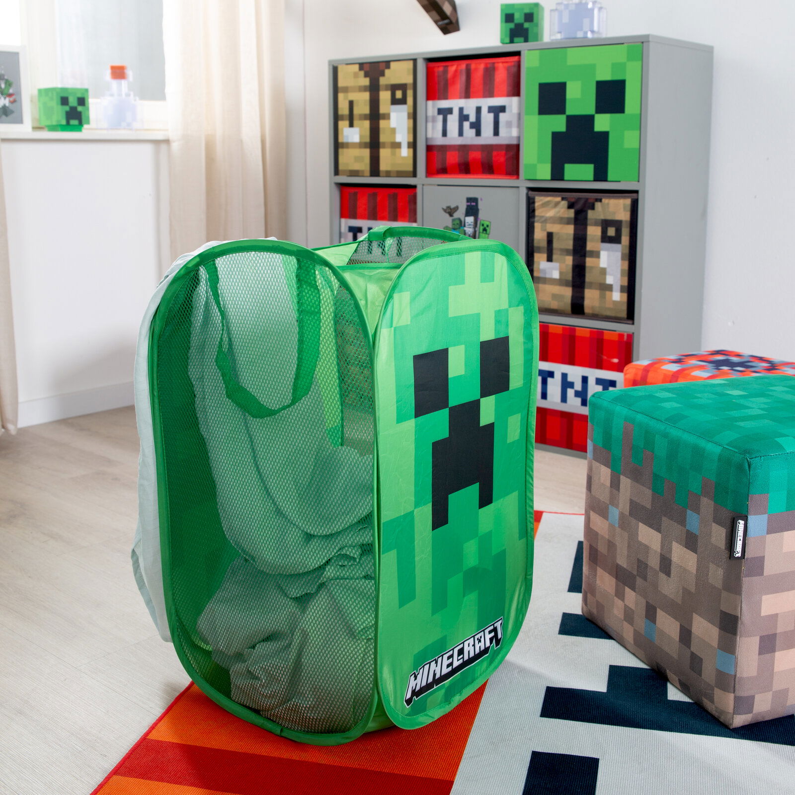 Grüner Minecraft Wäschekorb/Spielzeugkorb aus Mesh mit Creeper-Motiv und Tragegriffen, gefüllt mit Wäsche, im Kinderzimmer – Frontansicht leicht schräg von vorn.