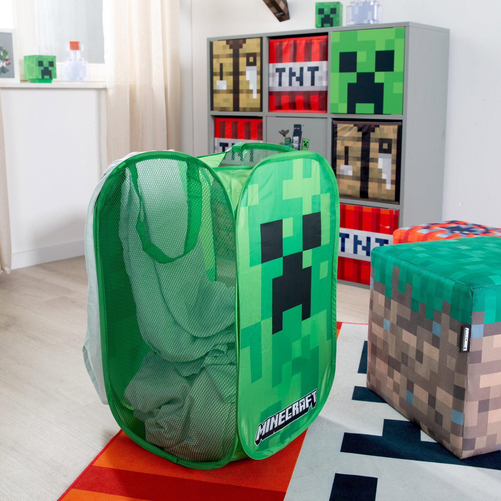 Grüner Minecraft Wäschekorb/Spielzeugkorb aus Mesh mit Creeper-Motiv und Tragegriffen, gefüllt mit Wäsche, im Kinderzimmer – Frontansicht leicht schräg von vorn.