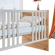 Babybett aus Holz mit weißen Gitterstäben, seitliche Perspektive