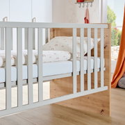 Babybett aus Holz mit weißen Gitterstäben, seitliche Perspektive