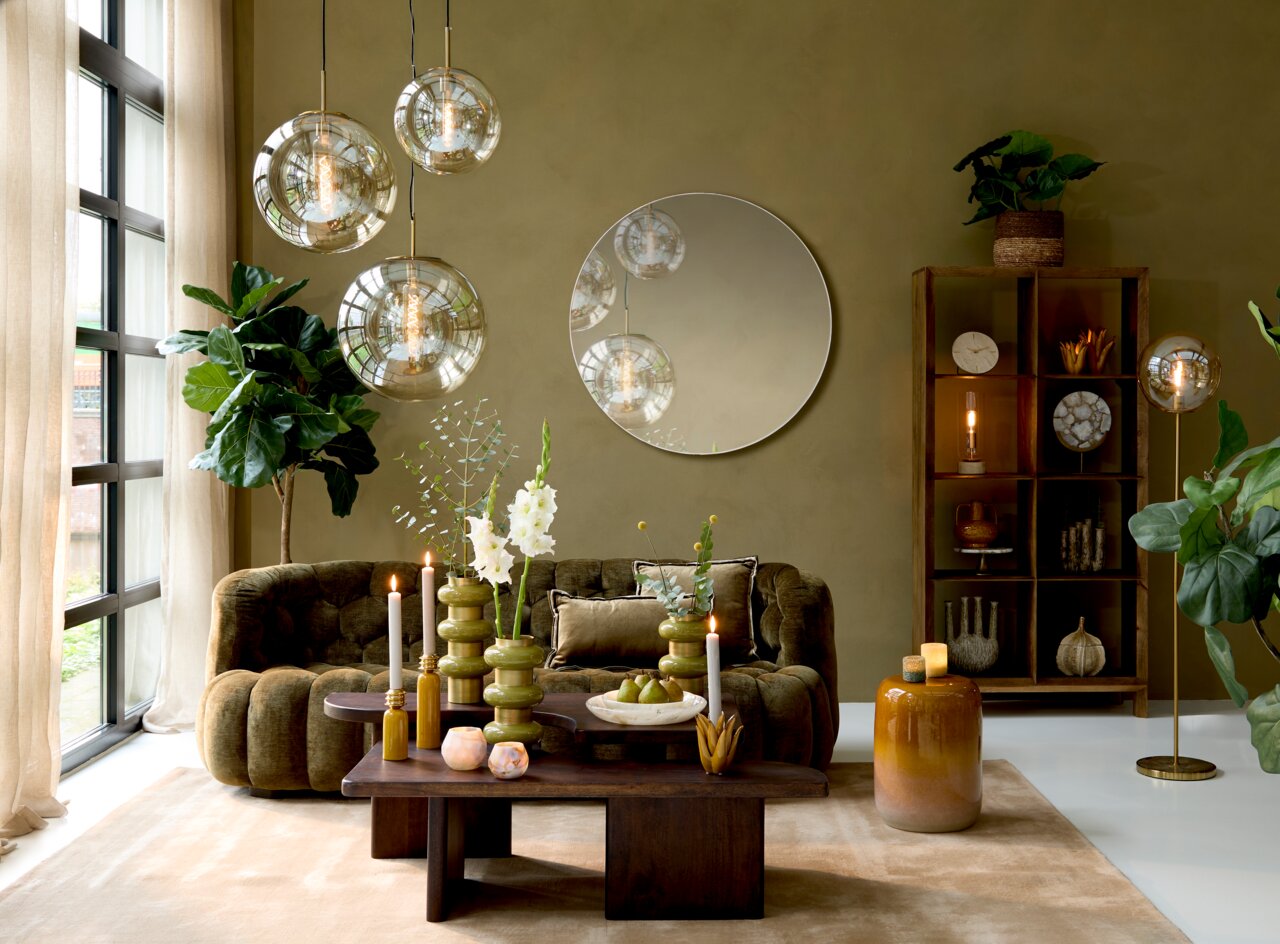 Moderner Couchtisch aus dunklem Holz in einem stilvoll eingerichteten Wohnzimmer mit grüner Couch, großen Pflanzen und eleganten Hängelampen. Perspektive von vorne.