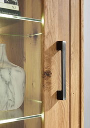 Nahaufnahme einer Vitrine aus Holz mit Glastür, Metallgriff und beleuchteten Glasregalen, Perspektive von der Seite.