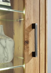 Nahaufnahme einer Vitrine aus Holz mit Glastür, Metallgriff und beleuchteten Glasregalen, Perspektive von der Seite.